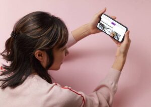 Eine Frau hält ihr Smartphone in beiden Händen und blickt auf den Bildschirm auf dem der Mini-Kurs Raus aus dem Hamsterrad zu sehen ist.